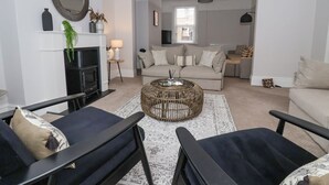 A modern living room with a fireplace, a sofa set, a coffee table, and a dining area visible through an archway. - Seascape Villa (Filey)