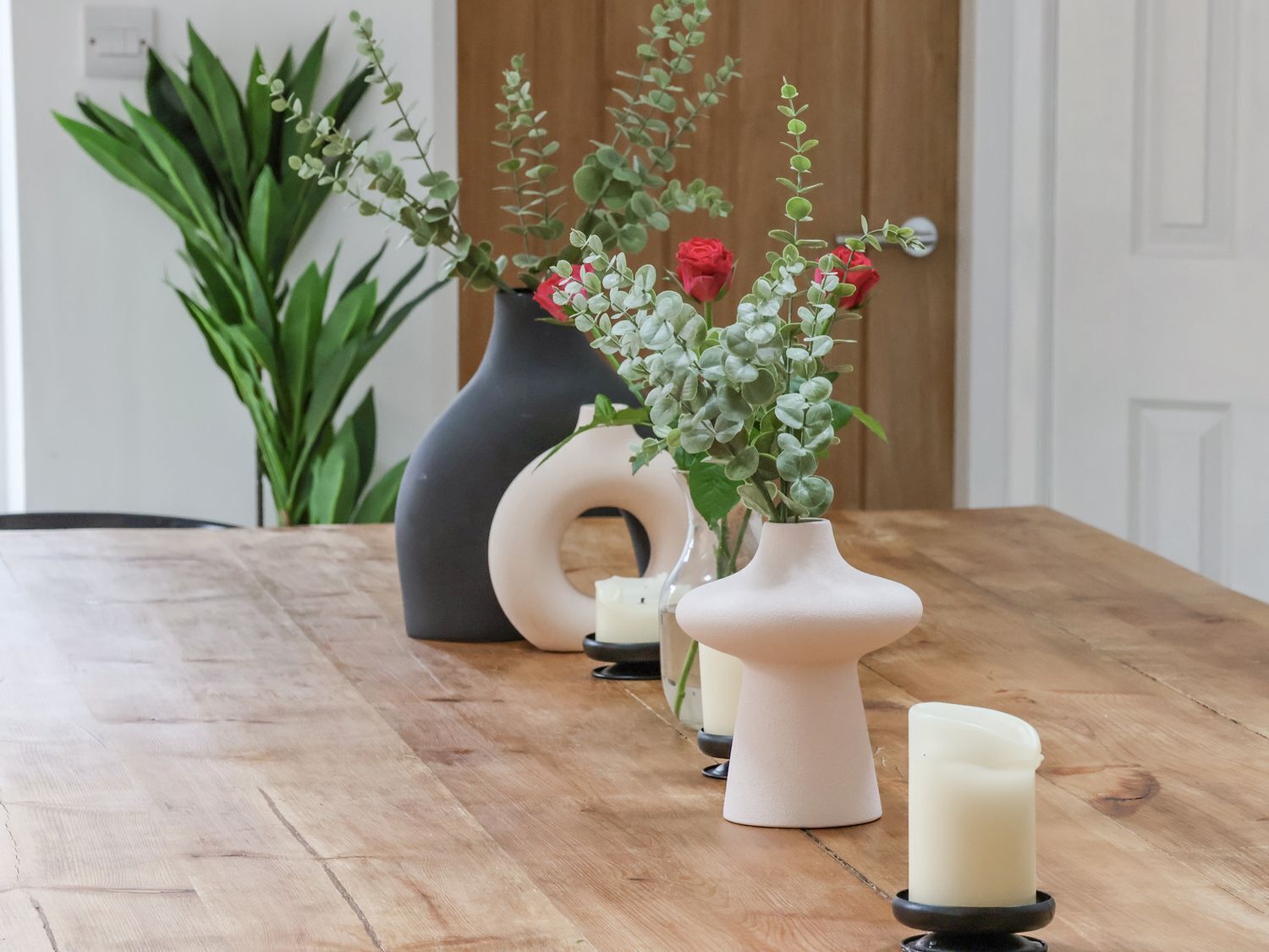A wooden dining table with three vases containing flowers and candles.