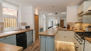 A modern kitchen with a central island, built-in appliances, and a view of the city through a window. - Seascape Villa (Filey)
