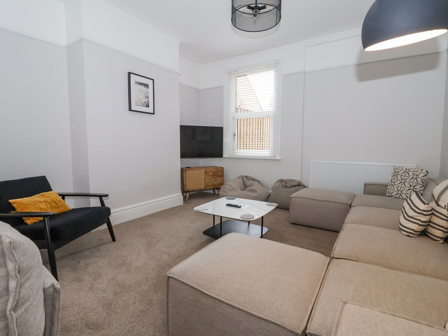 A modern living room with a black chair, beige sofa, and a white coffee table.
