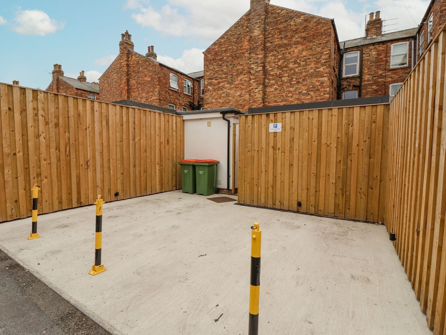 A fenced courtyard with a concrete floor, wooden fence, and two green bins.