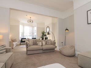 A living room with a beige sofa, a coffee table, and a bean bag chair. There is a floor lamp and a mirror on the wall. - Seascape Villa (Filey)