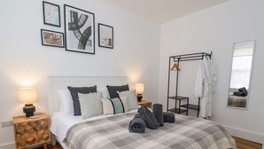 A modern bedroom with a large bed, two bedside tables, a hanging robe rack, and artwork on the wall. - Seascape Villa (Filey)
