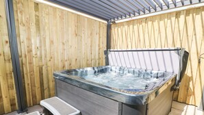 A hot tub with a wooden wall backdrop, a metal bench, and a small step leading into the tub. - Seascape Villa (Filey)