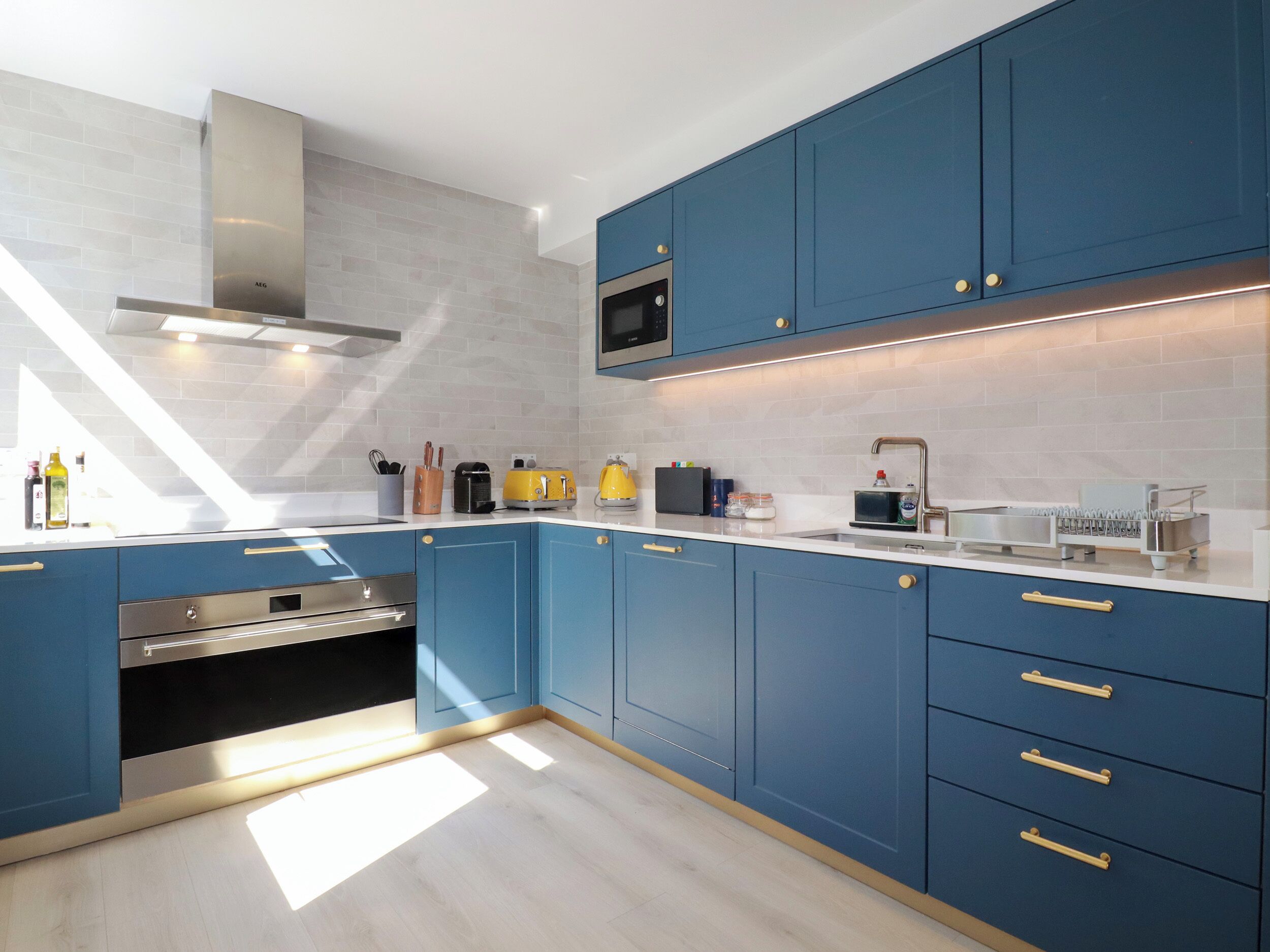 Une cuisine moderne avec des armoires bleues, une hotte de cuisinière en acier inoxydable, un four à micro-ondes et un four encastré.