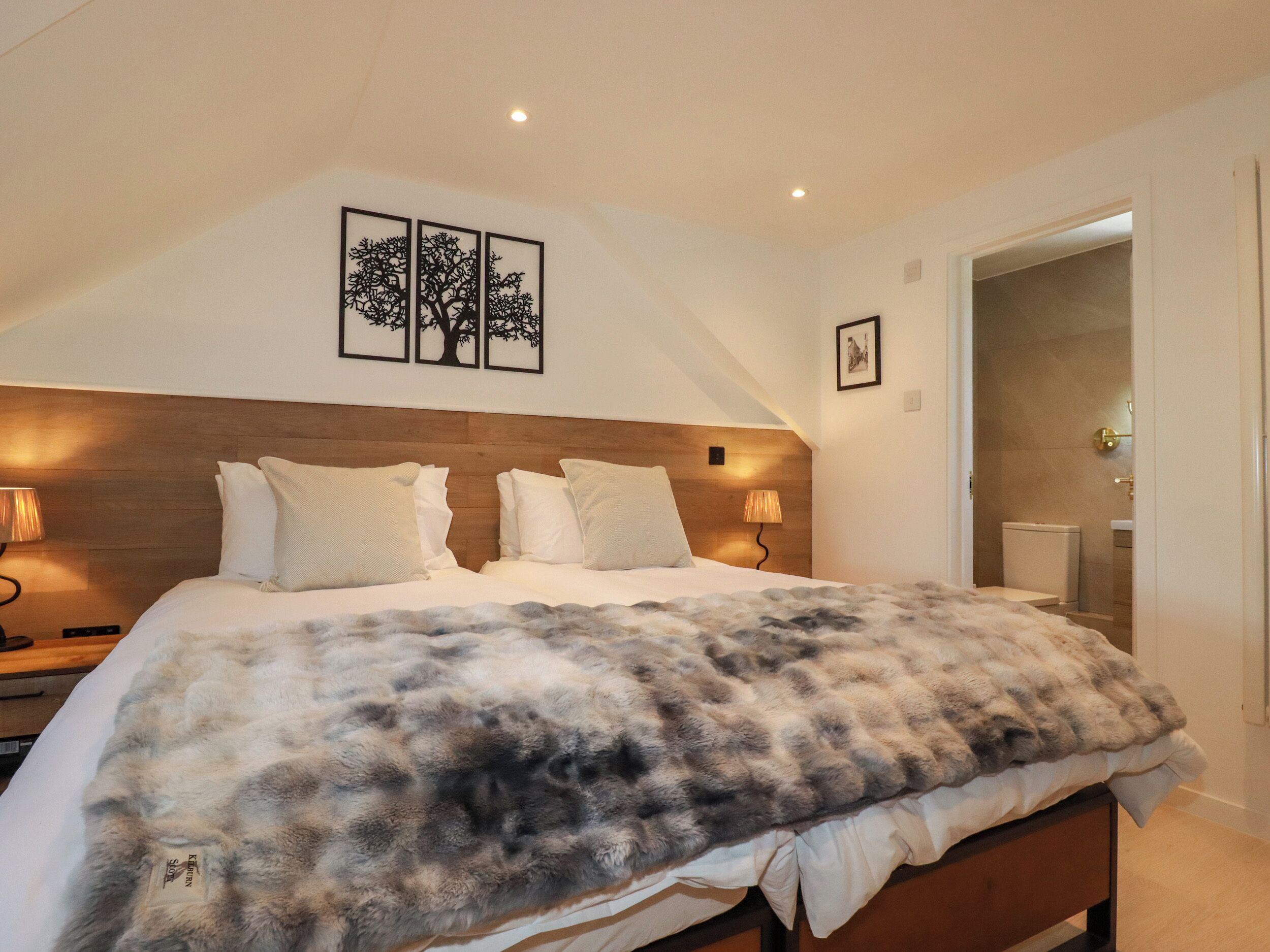 A bedroom with a large bed, two bedside lamps, a wooden headboard, and framed artwork on the wall.