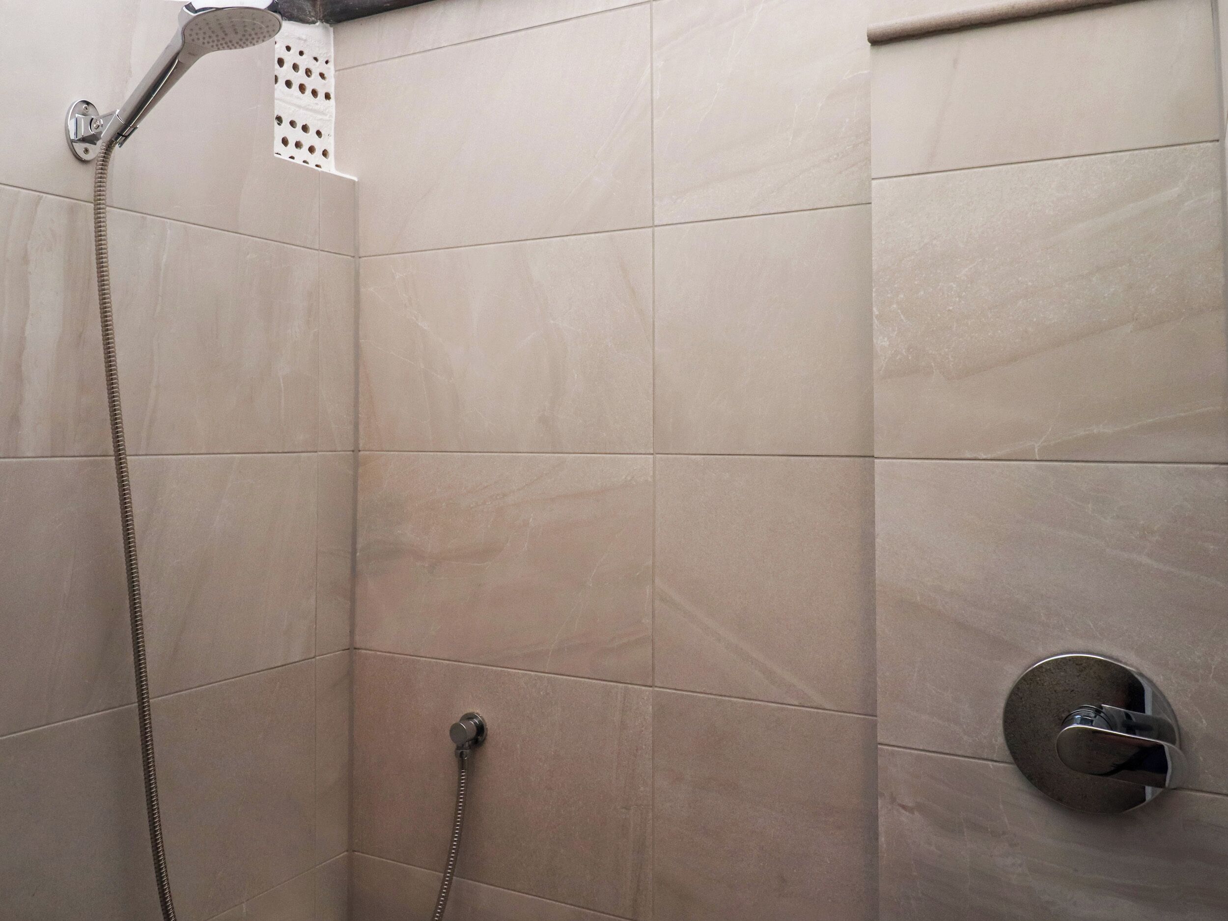 A shower area with a handheld showerhead and a wall-mounted faucet.