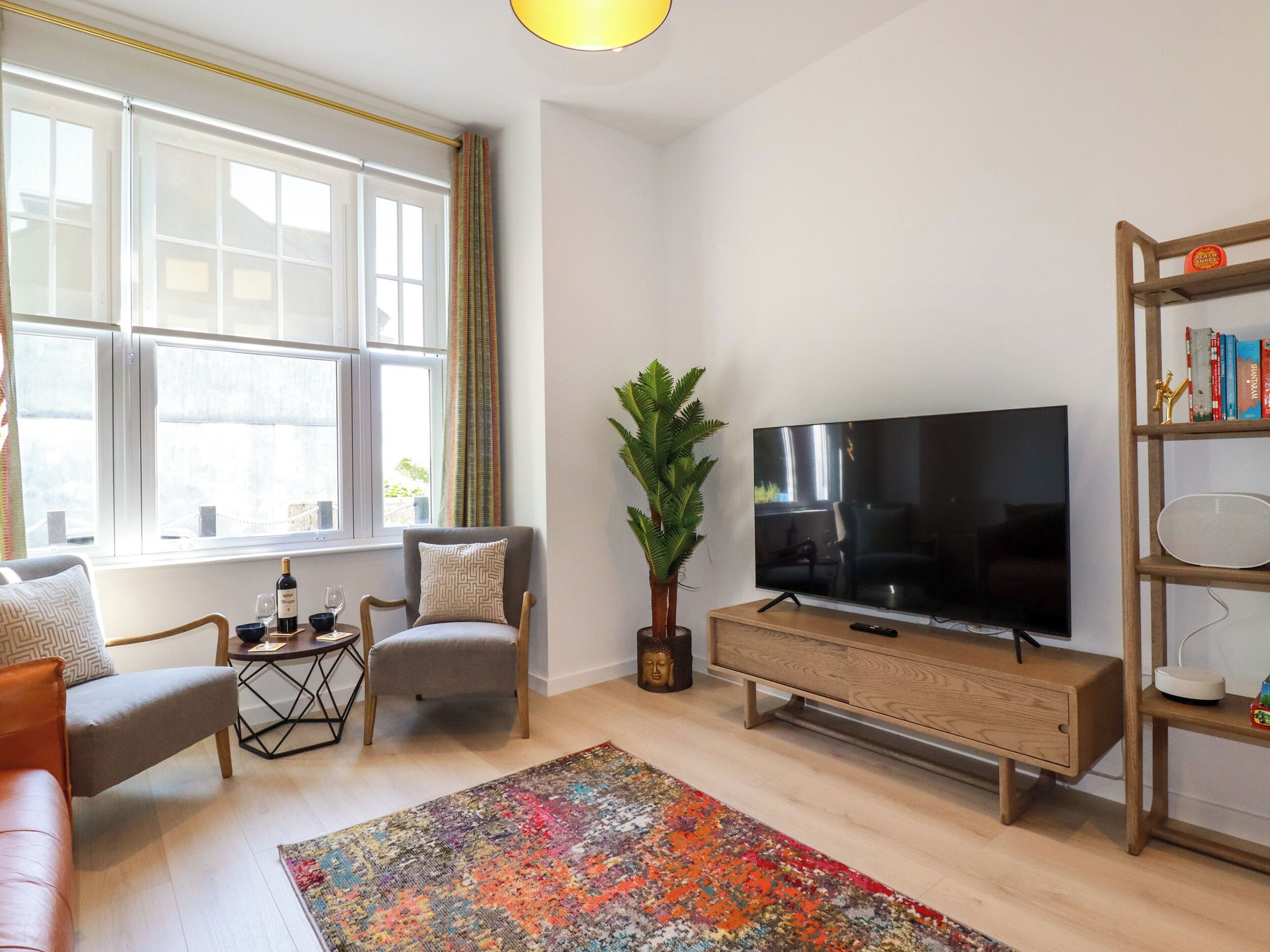 A living room with a large window, a sofa, a chair, a TV, a bookshelf, and a decorative Buddha statue.