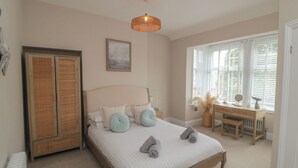 A bedroom with a bed, bedside table, lamp, and a window with blinds. - Thirty Four By the Sea (Scarborough)