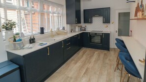 A modern kitchen with black cabinets, a white countertop, and a built-in oven. There is a window with blinds, a sink, and a plant on the counter. - Thirty Four By the Sea (Scarborough)