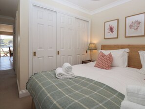 A bedroom with a bed, a green checkered bedspread, white pillows, a lamp, and framed botanical prints on the wall. - 6 Burgh Island (Kingsbridge)