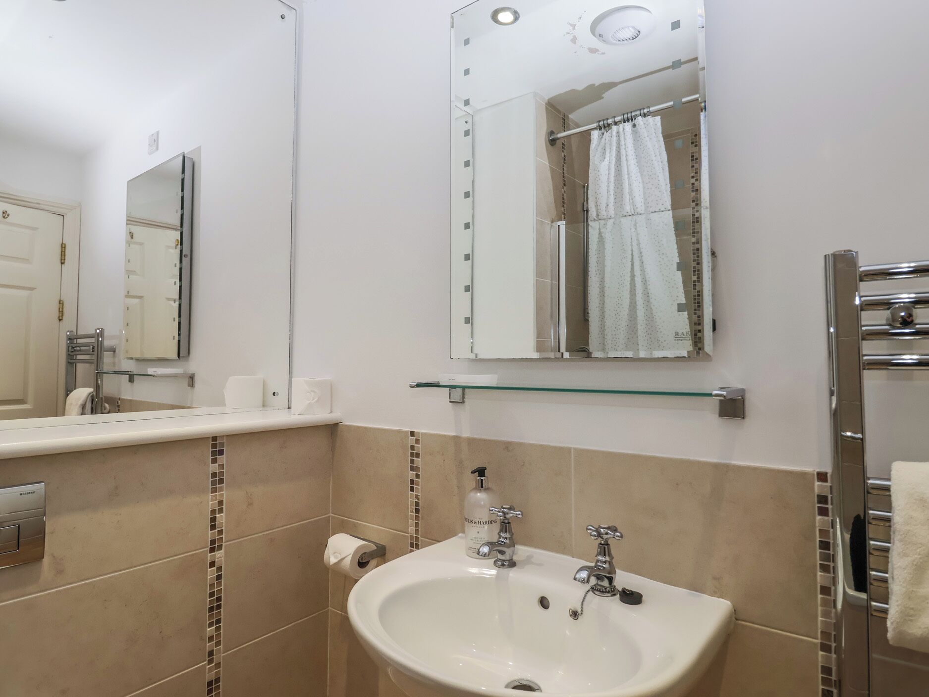 Un baño con lavamanos, espejo, toallero y cortina de ducha.