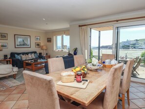 A dining area with a table set for four, a loaf of bread, a jar of jam, and a bowl of fruit. - 6 Burgh Island (Kingsbridge)