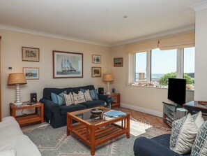 A living room with a sofa, coffee table, and TV, a window with a view, and framed pictures on the wall. - 6 Burgh Island (Kingsbridge)