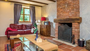 A cozy living room with a brick fireplace, a leather sofa, a glass coffee table, and a wooden cabinet. - Mill Cottage (Exeter)