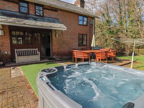 Une maison en briques avec un jacuzzi, une terrasse dotée d’une table et de chaises, et une pelouse.