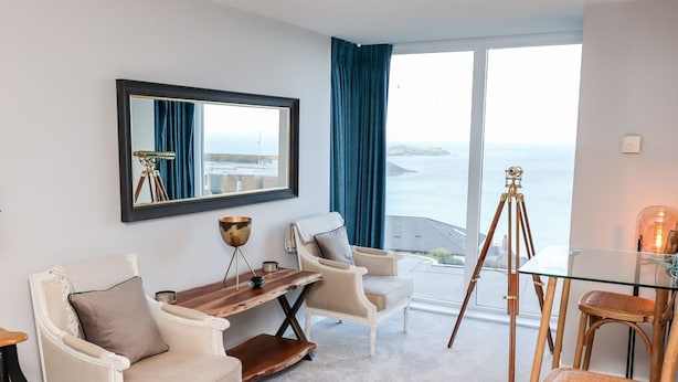 Ett modernt vardagsrum med utsikt över havet, inrett med en soffa, fåtöljer, ett soffbord och ett stativ.