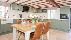 A kitchen with green cabinets, a wooden dining table with chairs, and a built-in microwave. - 3 Trem y Mor (Holyhead)