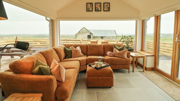 A spacious living area with a large sofa, a coffee table, and a view of the countryside. - 3 Trem y Mor (Holyhead)