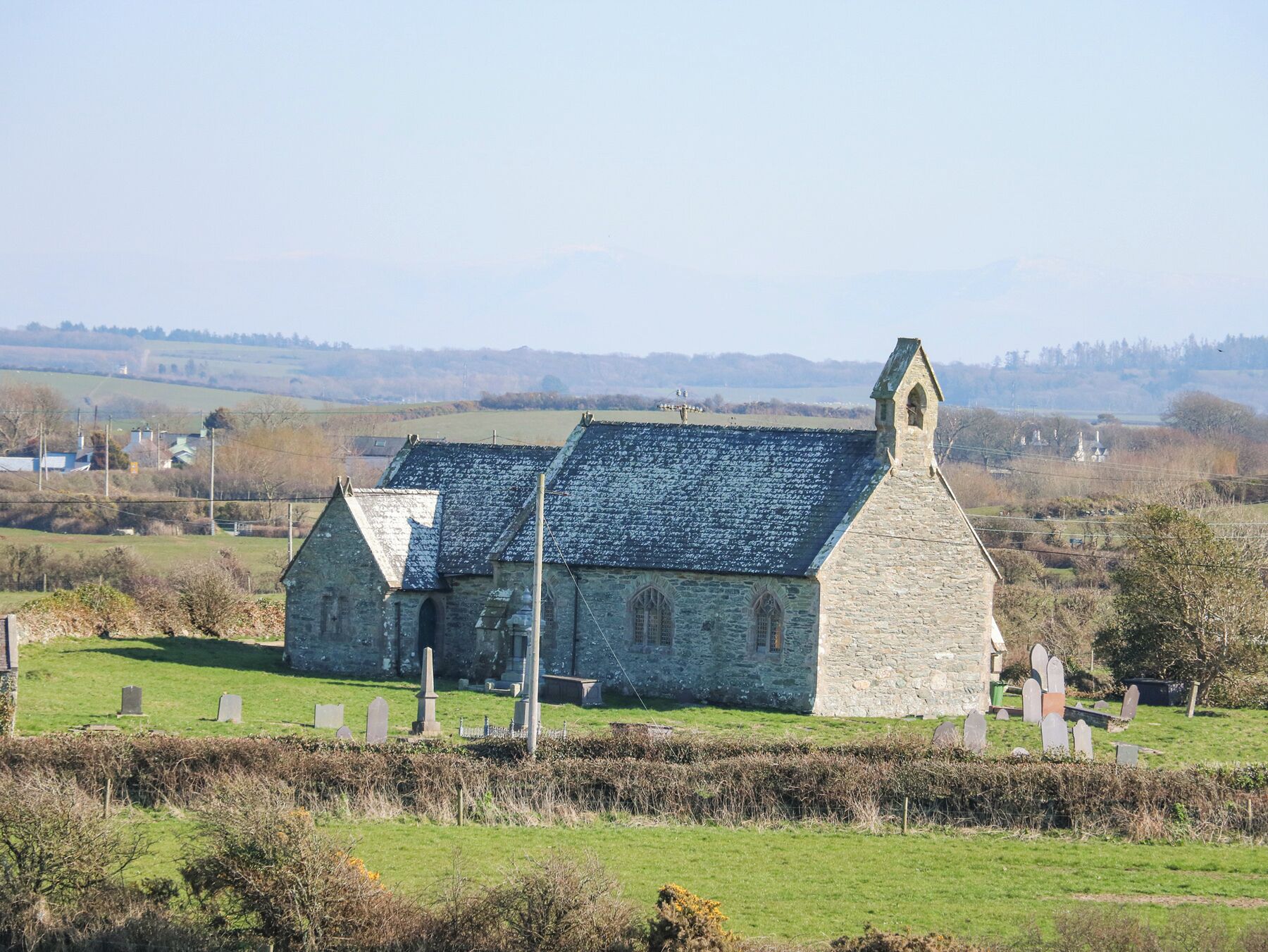 A stone church with a steeply pitched roof and a bell tower, surrounded by a cemetery with headstones.
