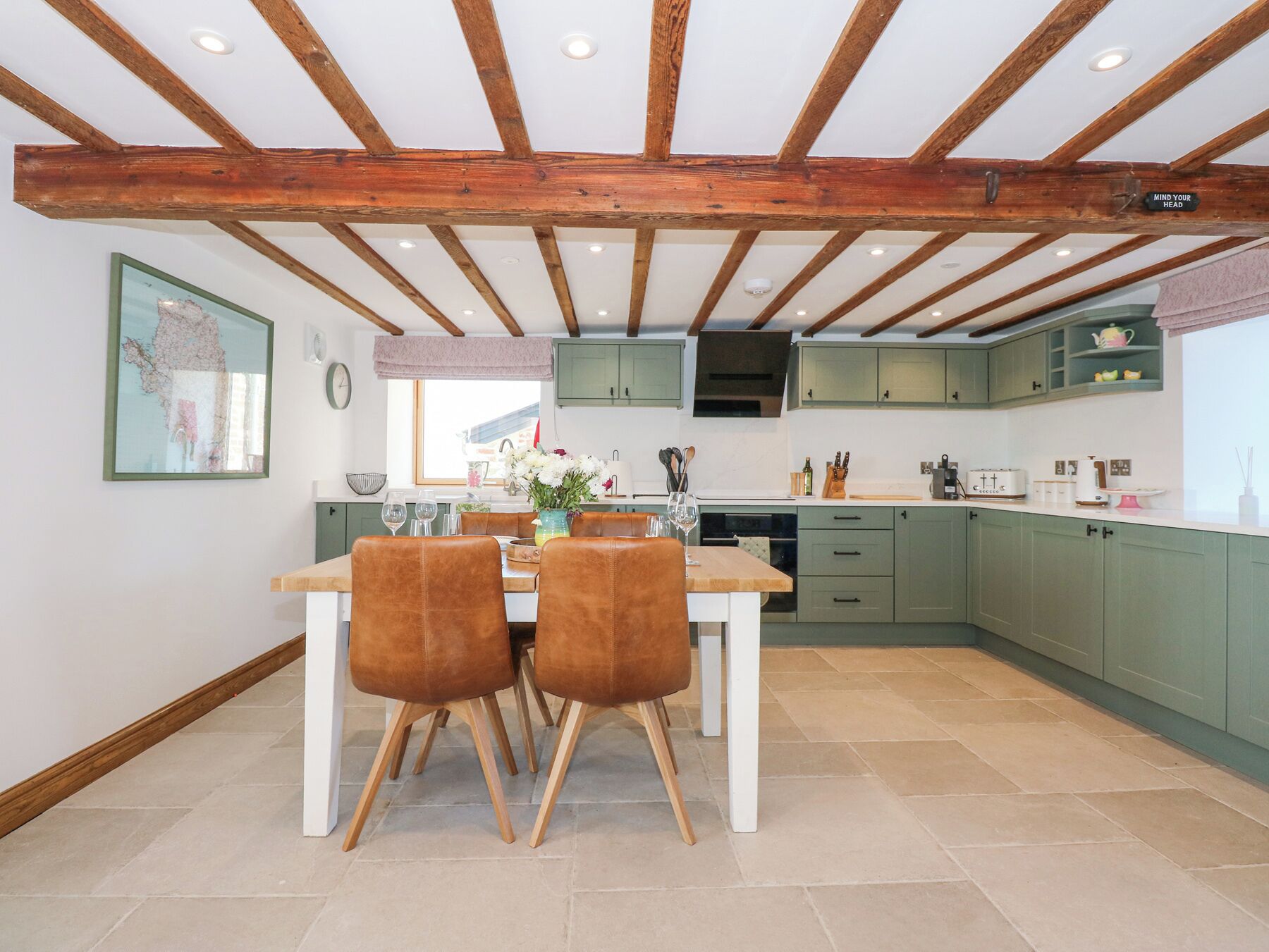 A kitchen with wooden beams, green cabinets, and a dining area with chairs and a table.