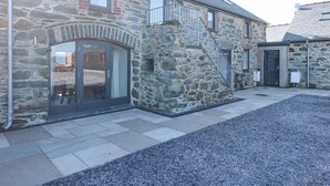 A stone building with a large glass door, a staircase leading to a second floor, and a gravel driveway. - 3 Trem y Mor (Holyhead)