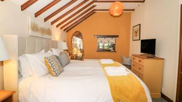 A bedroom with a large bed, wooden beams on the ceiling, a mirror, a window with a view, a television, and a dresser.