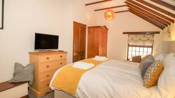 A bedroom with a bed, a television on a wooden dresser, a window with curtains, and a wooden ceiling.