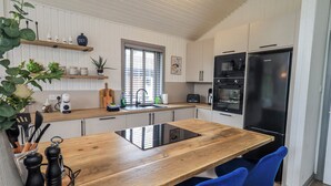 A modern kitchen with a wooden table, blue chairs, a black refrigerator, and white cabinets. - Fig Tree Lodge (Penrith)