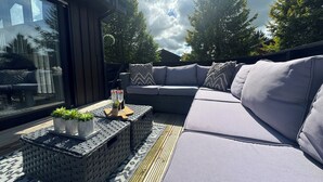 A modern outdoor seating area with a cushioned sofa, a small table with drinks, and a view of the sky and trees. - Fig Tree Lodge (Penrith)
