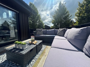 A modern outdoor seating area with a cushioned sofa, a small table with drinks, and a view of the sky and trees. - Fig Tree Lodge (Penrith)
