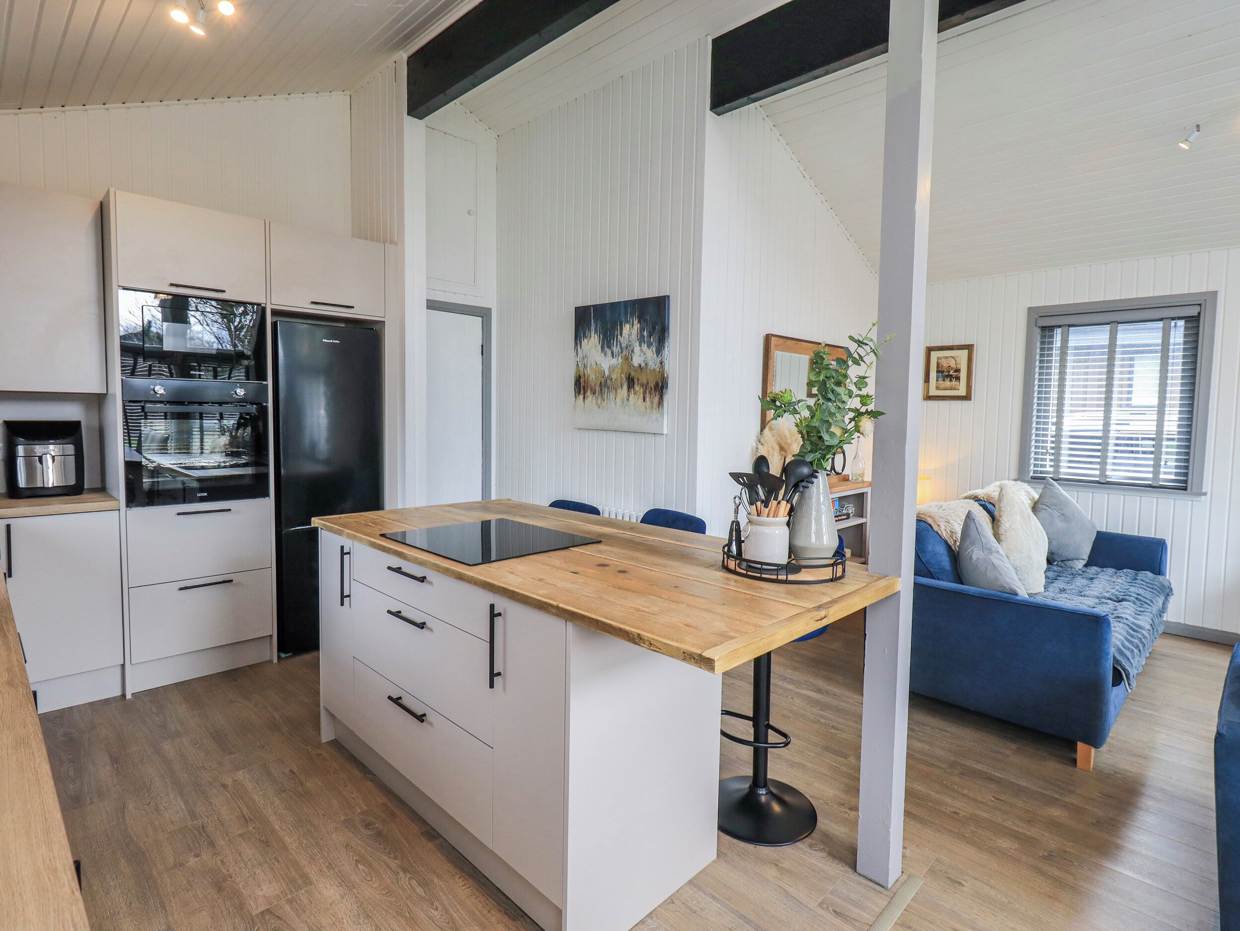 Una cocina moderna con una isla central, muebles blancos y un refrigerador negro.
