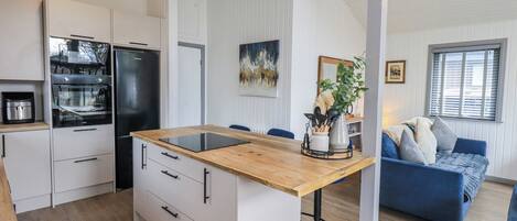Una cocina moderna con una isla central, muebles blancos y un refrigerador negro.