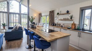 A modern kitchen with a wooden island, bar stools, and a dining area with a sofa and chairs. - Fig Tree Lodge (Penrith)
