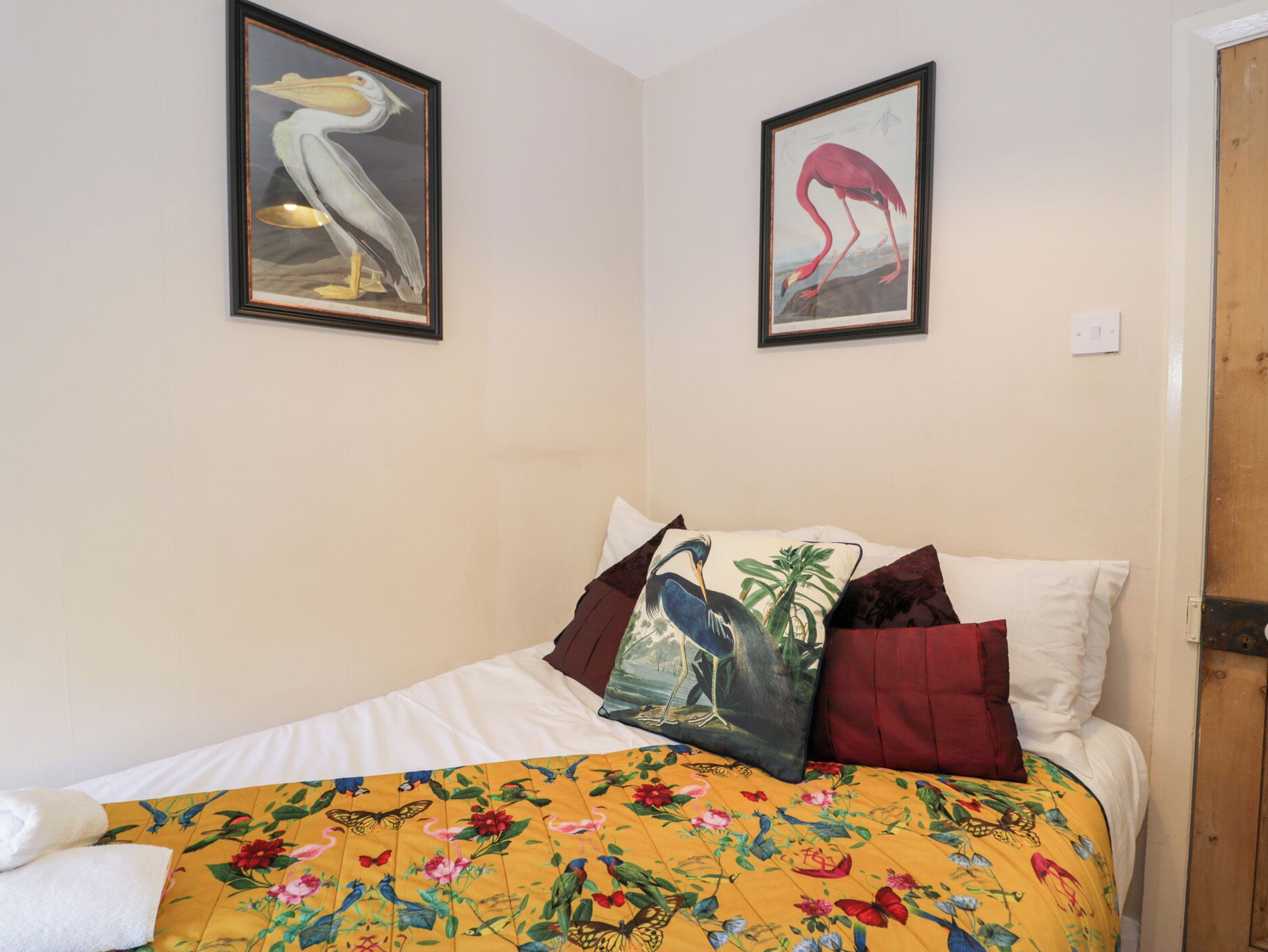 A bed with a floral bedspread, white pillows, and a framed bird painting above it.