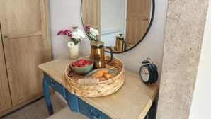 A bathroom with a wooden cabinet, a mirror, a wall-mounted clock, and a wicker basket containing strawberries, croissants, and a coffee pot. - Hollywood Cottage (Barnard Castle)