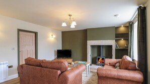 A living room with two brown sofas, a television, a fireplace, and a stone wall. - Hollywood Cottage (Barnard Castle)