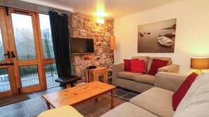 Ein Wohnzimmer mit einer Steinwand, einem Sofa, einem Holztisch und einem an der Wand befestigten Fernseher.