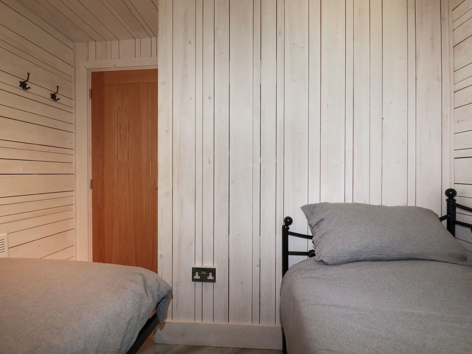 Une chambre avec deux lits simples, des murs recouverts de panneaux de bois, une porte en bois et une prise électrique sur le mur.