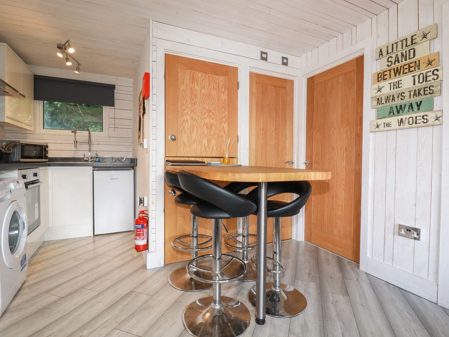 A compact kitchen with a washing machine, a microwave, and a sink. There are two wooden doors and a sign on the wall.