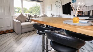 Una cocina moderna con una mesa de madera, taburetes negros, un sofá y un ventanal grande.