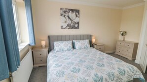 Une chambre à coucher comprenant un lit, deux tables de chevet, une commode, un radiateur, une fenêtre avec des rideaux et une œuvre d’art accrochée au mur.