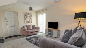 A living room with a sofa, a coffee table, a television on a stand, and a door.
