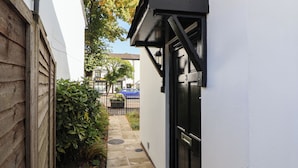 A narrow alleyway with a black door marked with the number 3, a white building, and a wooden fence on the left.