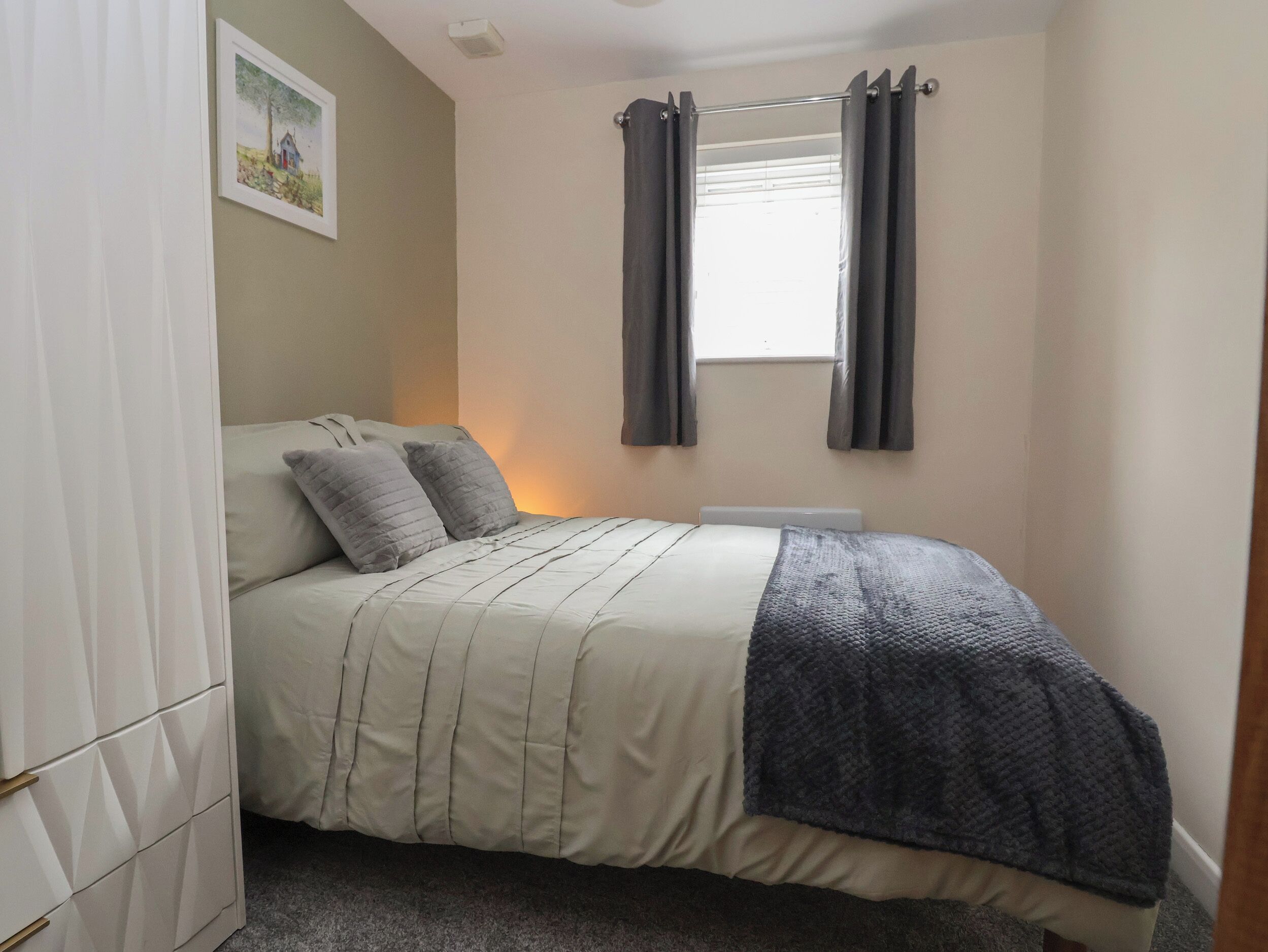A bedroom with a bed, a wardrobe, a window with curtains, and a painting on the wall.