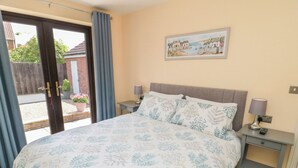 A bedroom with a bed, two bedside tables, a nightstand, a painting, and a view through a glass door. - 6 Fairfax Close (York)