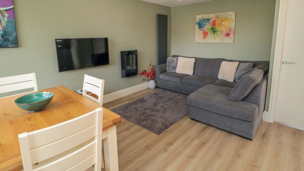 A living room with a grey sofa, a wooden dining table with chairs, a flat-screen TV, and a colorful abstract painting on the wall. - 6 Fairfax Close (York)