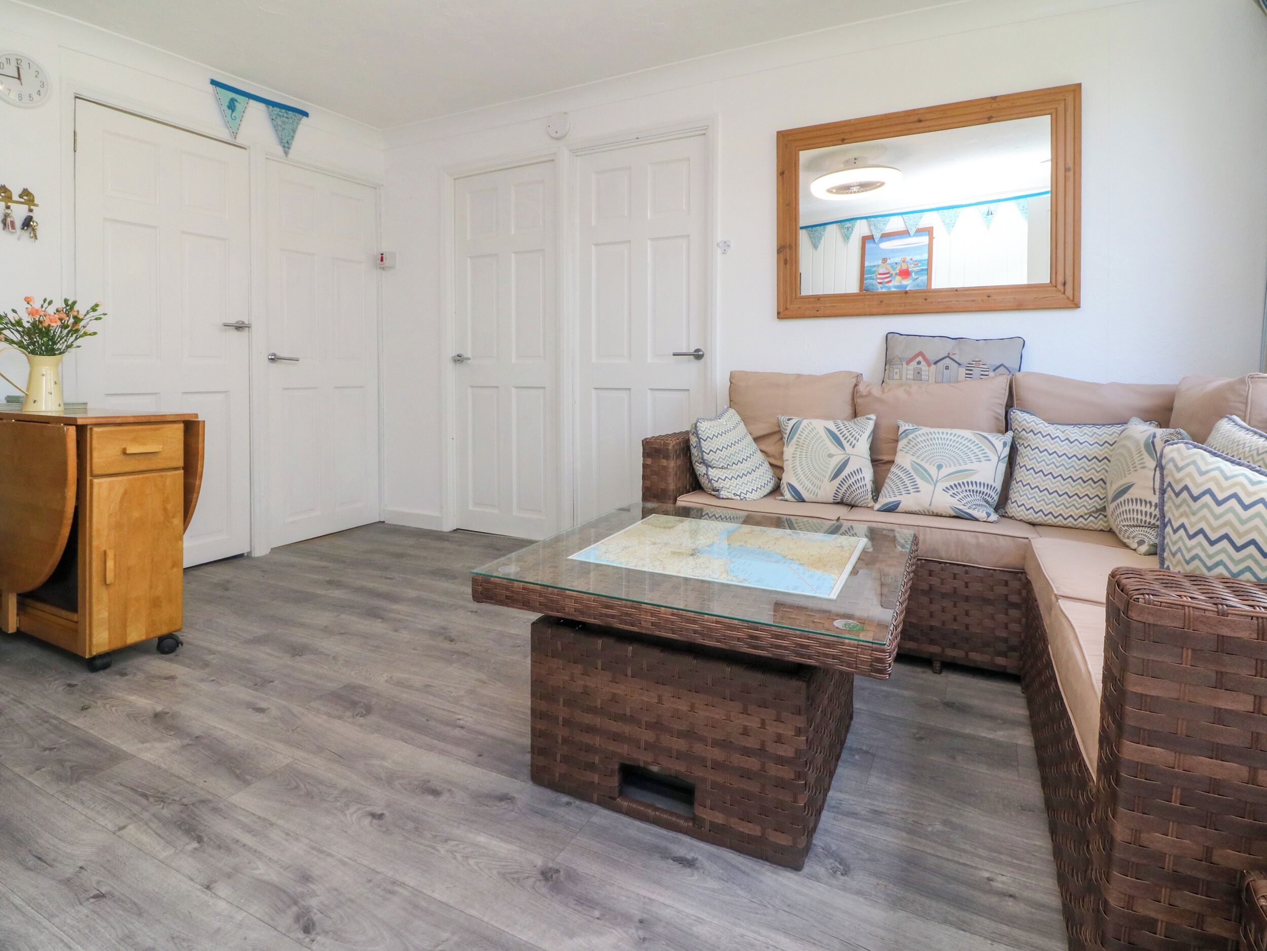 Ein Wohnzimmer mit Glastisch, Korbmöbeln, einer Couch mit gemusterten Kissen und einem Holzschrank.