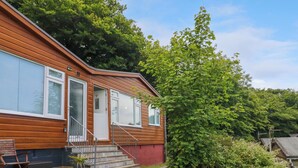 A two-story wooden house with a front porch, a small garden, and a staircase leading to the entrance. - 4 The Park (Bude)