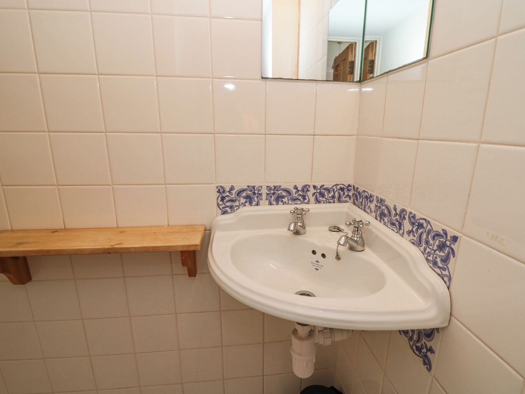 A bathroom with a white sink, two faucets, a wooden shelf, and blue patterned tiles.